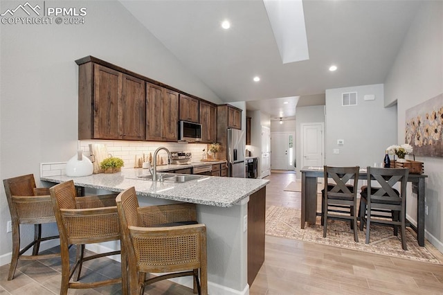 kitchen with kitchen peninsula, light stone counters, a breakfast bar, stainless steel appliances, and sink