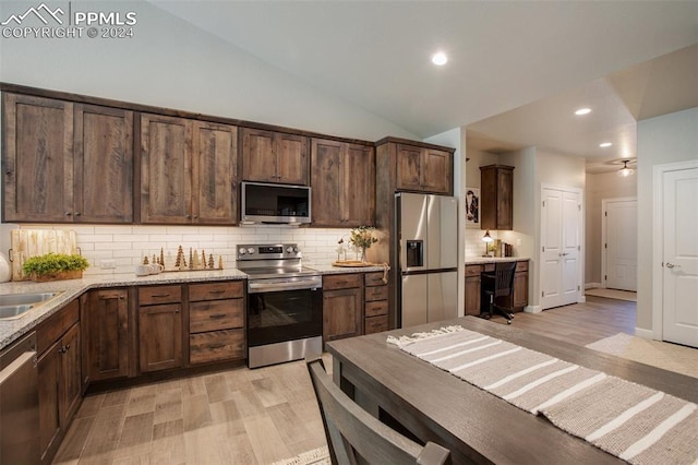 kitchen with vaulted ceiling, decorative backsplash, light wood-type flooring, light stone countertops, and stainless steel appliances