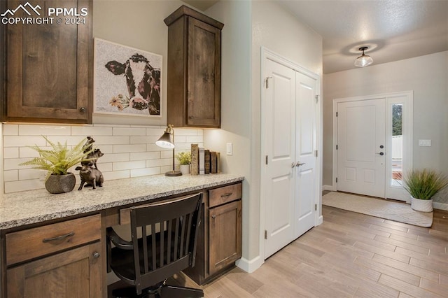 kitchen with built in desk, light wood-type flooring, tasteful backsplash, light stone counters, and dark brown cabinetry