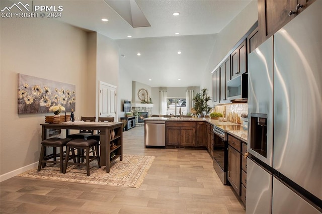 kitchen with kitchen peninsula, light stone countertops, light wood-type flooring, stainless steel appliances, and sink