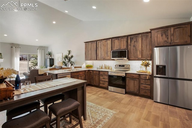 kitchen with backsplash, stainless steel appliances, vaulted ceiling, sink, and light hardwood / wood-style floors