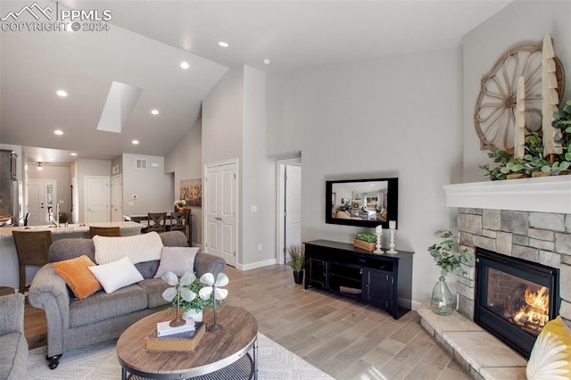 living room with light hardwood / wood-style floors, a stone fireplace, high vaulted ceiling, and a skylight