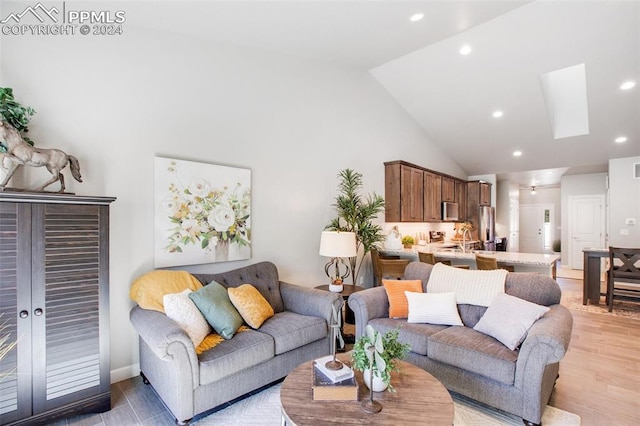 living room with light wood-type flooring, sink, high vaulted ceiling, and a skylight