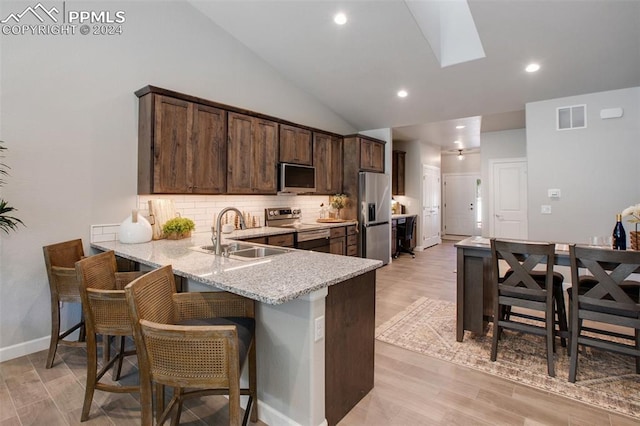 kitchen with kitchen peninsula, light stone counters, stainless steel appliances, sink, and light hardwood / wood-style floors