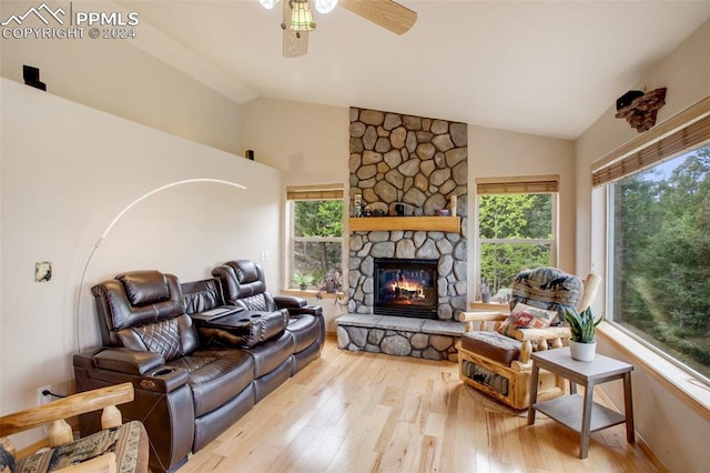 living room with lofted ceiling, a stone fireplace, ceiling fan, and light wood-type flooring