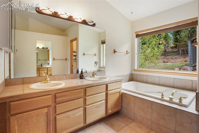 bathroom with lofted ceiling, vanity, tile patterned flooring, and tiled bath