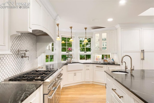 kitchen featuring white cabinets, sink, high end stove, and hanging light fixtures