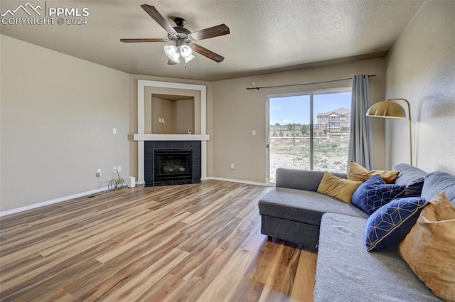 living room with a textured ceiling, ceiling fan, wood-type flooring, and a fireplace