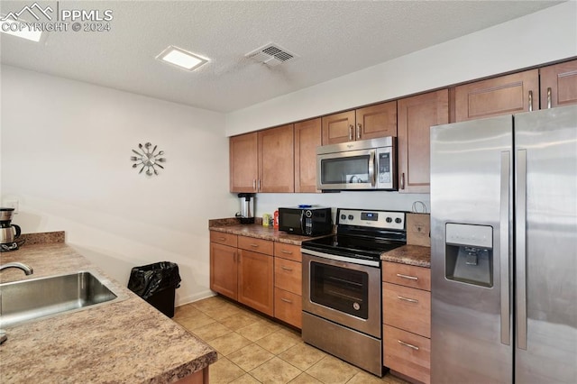 kitchen with sink, light tile patterned flooring, a textured ceiling, and appliances with stainless steel finishes