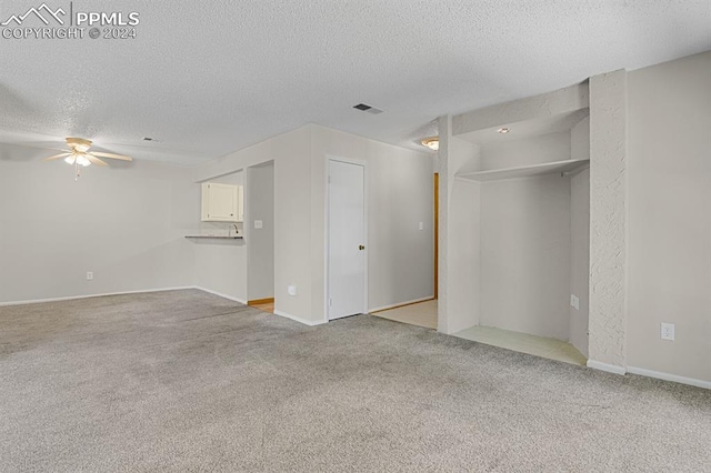 unfurnished living room featuring ceiling fan, light colored carpet, and a textured ceiling