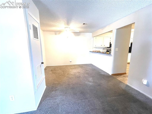 unfurnished living room featuring light carpet, ceiling fan, and a textured ceiling