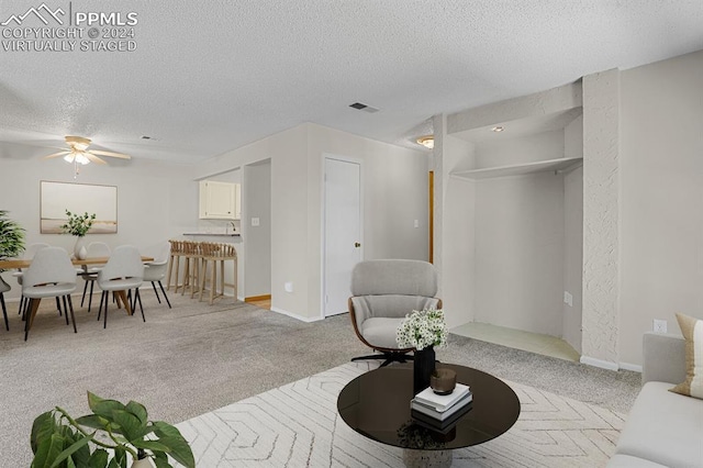 carpeted living room featuring ceiling fan and a textured ceiling