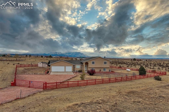 view of front of house with a rural view, a mountain view, a garage, and a front lawn