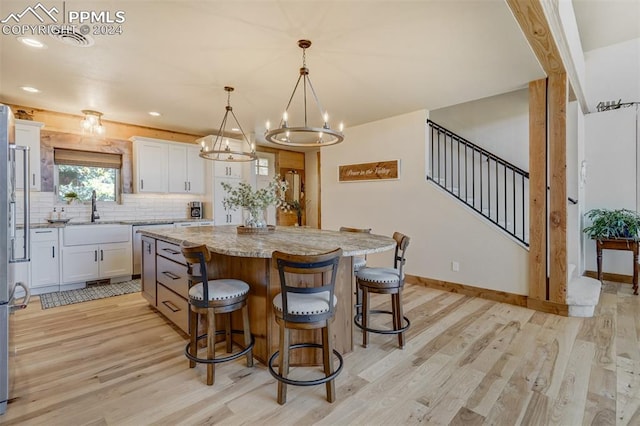 kitchen featuring a center island, white cabinetry, light hardwood / wood-style floors, light stone counters, and pendant lighting