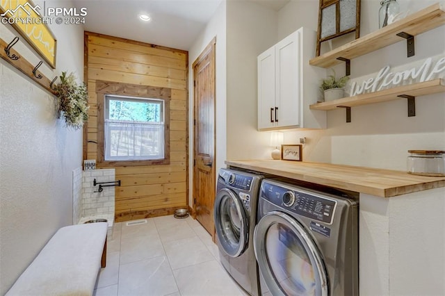 washroom with light tile floors, independent washer and dryer, cabinets, and wood walls