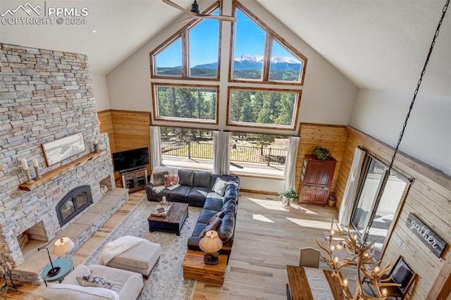 living room featuring a fireplace, ceiling fan, high vaulted ceiling, wood-type flooring, and wooden walls