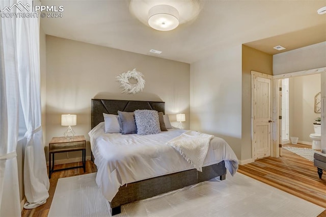 bedroom with ensuite bathroom and hardwood / wood-style floors