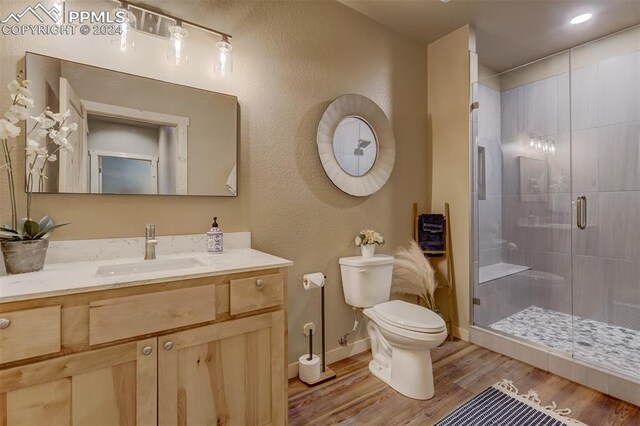 bathroom with walk in shower, vanity with extensive cabinet space, toilet, and hardwood / wood-style floors