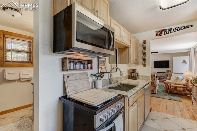 kitchen with stainless steel appliances, sink, light brown cabinetry, and light tile floors