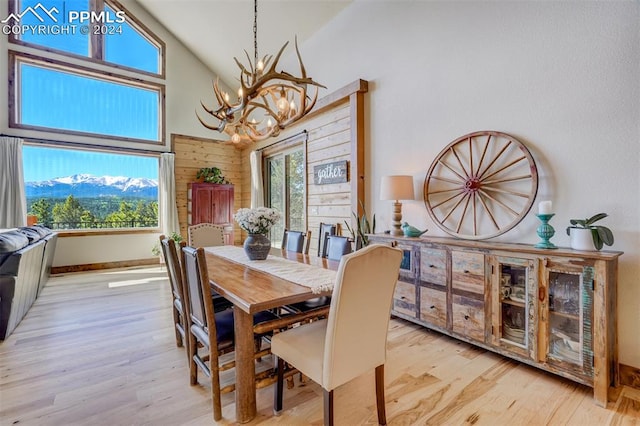 dining space featuring a notable chandelier, high vaulted ceiling, wooden walls, and light hardwood / wood-style flooring