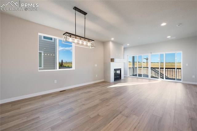 unfurnished living room featuring a tiled fireplace, a healthy amount of sunlight, and light wood-type flooring