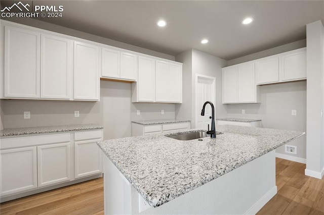 kitchen featuring a kitchen island with sink, sink, light stone counters, and white cabinets