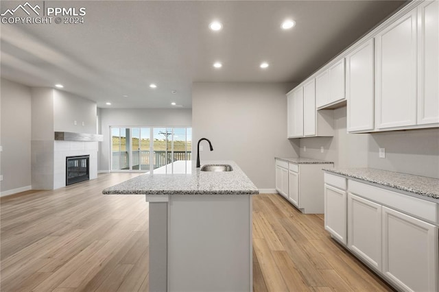 kitchen featuring an island with sink, sink, white cabinets, and light stone counters