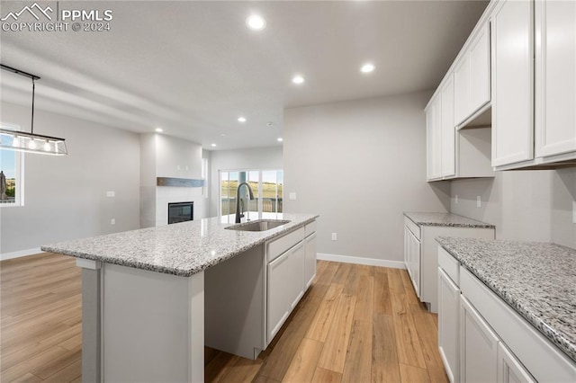 kitchen featuring decorative light fixtures, an island with sink, sink, white cabinets, and light wood-type flooring