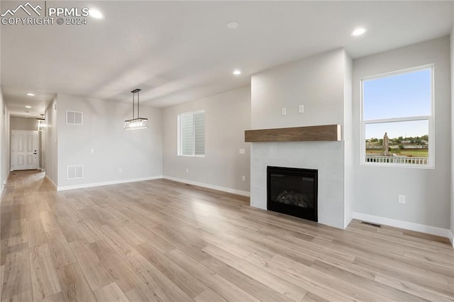 unfurnished living room with a tiled fireplace and light hardwood / wood-style floors