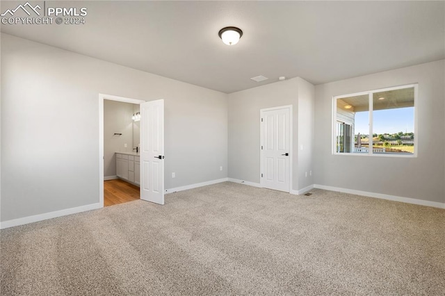 unfurnished bedroom featuring light carpet and ensuite bath