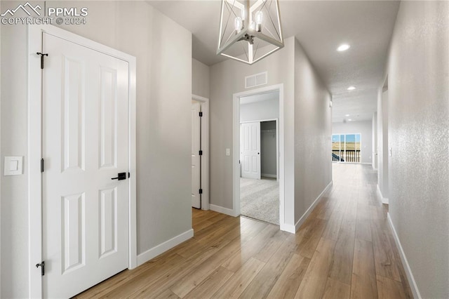 hallway with an inviting chandelier and light hardwood / wood-style floors