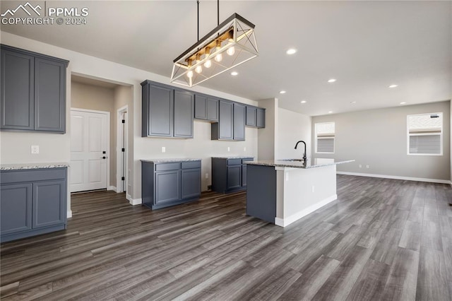 kitchen featuring a center island with sink, decorative light fixtures, dark hardwood / wood-style floors, light stone countertops, and a kitchen breakfast bar