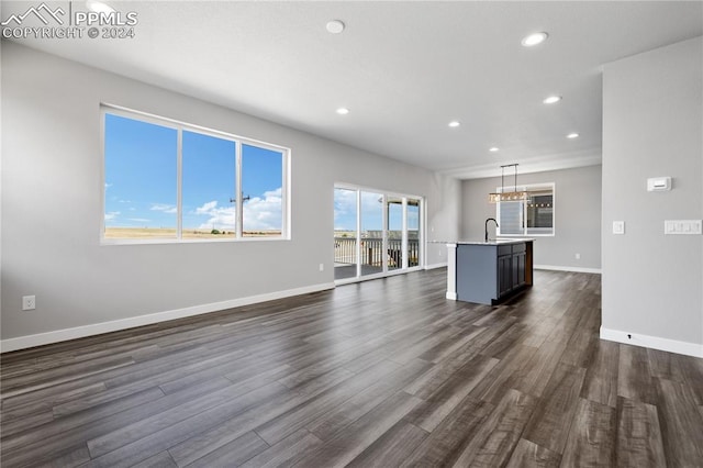 unfurnished living room featuring sink, an inviting chandelier, and dark wood-type flooring