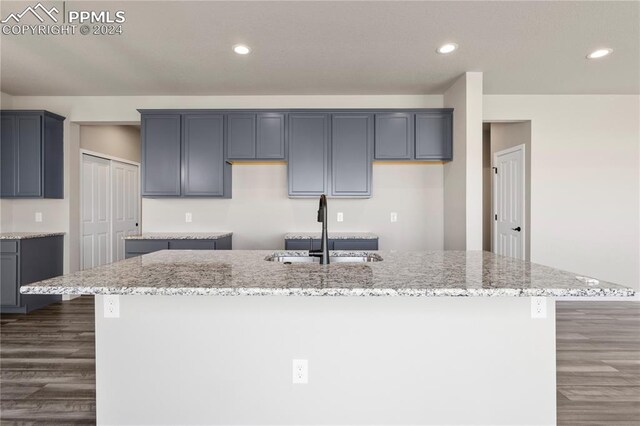 kitchen with dark wood-type flooring, light stone counters, an island with sink, sink, and gray cabinetry