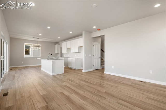 kitchen featuring sink, hanging light fixtures, light wood-type flooring, an island with sink, and white cabinetry