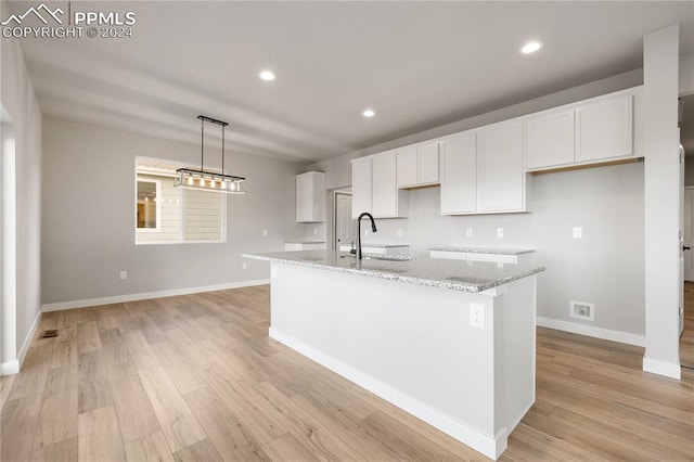 kitchen featuring white cabinetry, sink, light stone countertops, a center island with sink, and light hardwood / wood-style floors