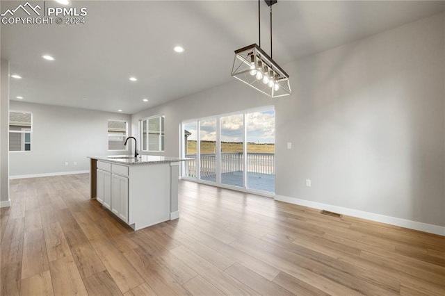 kitchen featuring a center island with sink, white cabinetry, pendant lighting, and light wood-type flooring