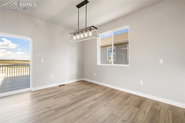 unfurnished dining area with a notable chandelier, light wood-type flooring, and plenty of natural light