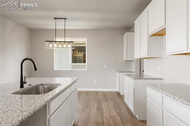 kitchen with pendant lighting, white cabinets, light wood-type flooring, sink, and light stone counters