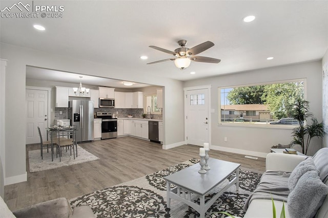 living room with sink, light hardwood / wood-style floors, and ceiling fan with notable chandelier