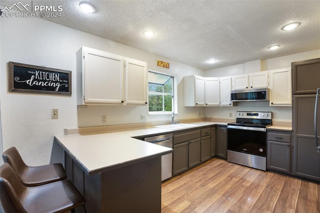 kitchen with a textured ceiling, white cabinetry, sink, kitchen peninsula, and stainless steel appliances