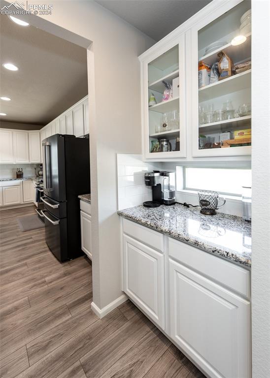 kitchen featuring white cabinets, black fridge, decorative backsplash, light wood-type flooring, and light stone counters