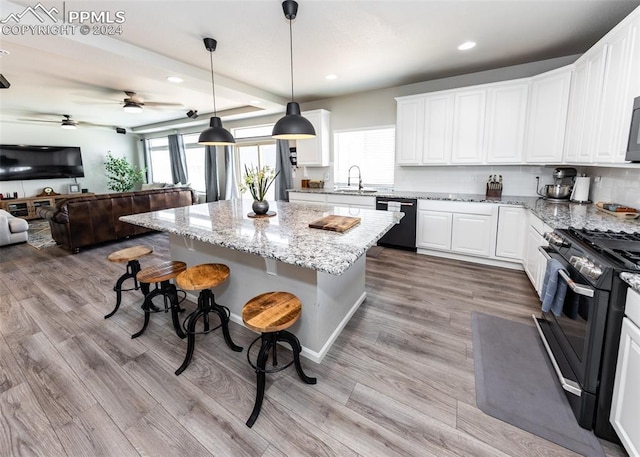 kitchen featuring a kitchen bar, a kitchen island, black dishwasher, white cabinetry, and stainless steel range with gas stovetop