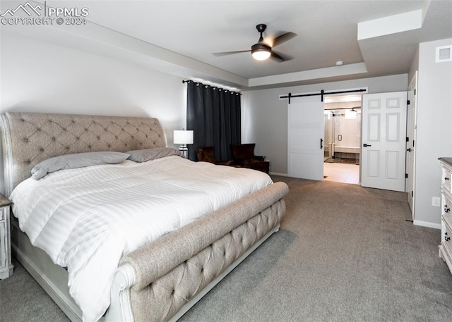 bedroom with light carpet, ensuite bath, a tray ceiling, ceiling fan, and a barn door