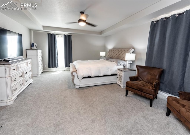 carpeted bedroom featuring a raised ceiling, multiple windows, and ceiling fan