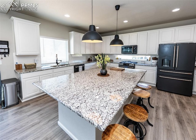 kitchen featuring sink, a center island, a breakfast bar area, white cabinets, and black appliances