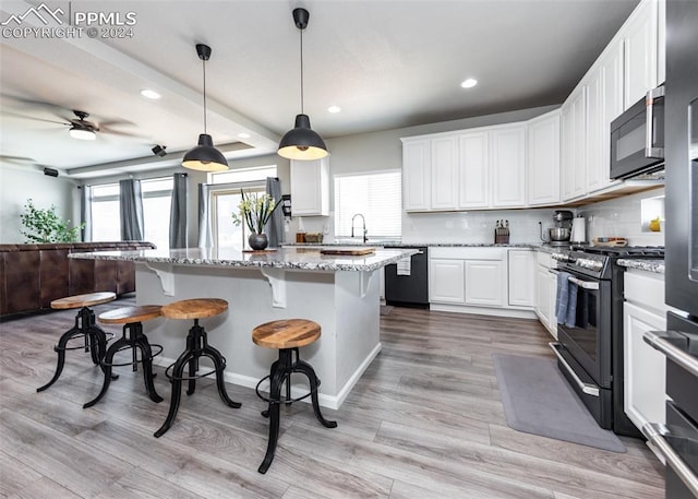 kitchen with white cabinets, light stone counters, stainless steel stove, and decorative light fixtures