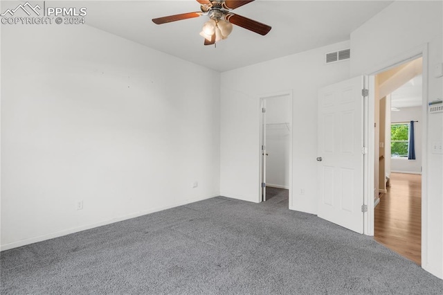 unfurnished bedroom with ceiling fan, a closet, a spacious closet, and dark colored carpet