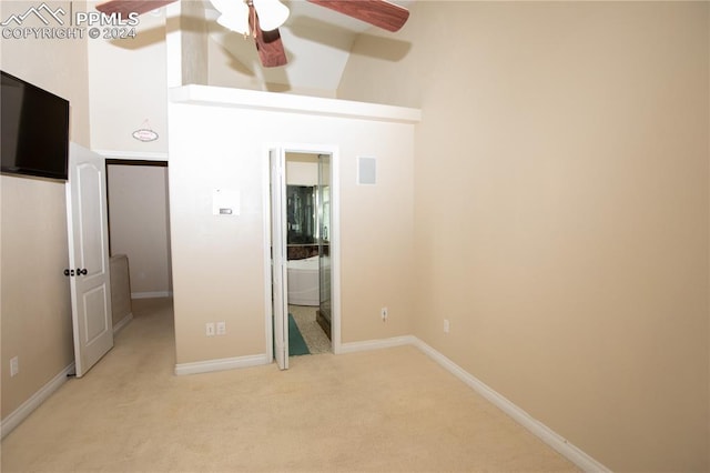 unfurnished bedroom with ceiling fan, light colored carpet, and a high ceiling