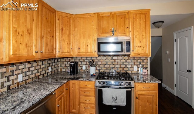 kitchen with dark hardwood / wood-style floors, dark stone countertops, stainless steel appliances, and tasteful backsplash